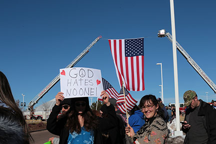 A woman holds up a sign saying God hates no one. Accompanied by her friend. 