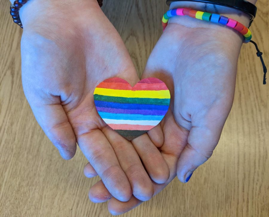 Gay Straight Trans Alliance Vice President, Ari Clark, holds a rainbow heart in their hand as a symbol of support for the LGBTQ+ community.
