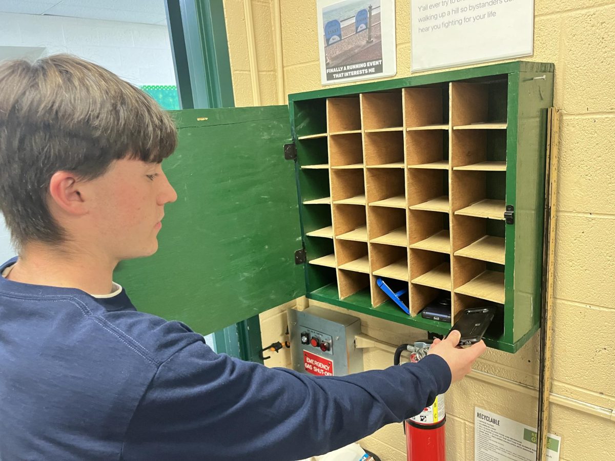 Kyle Blasi (11) puts his phone in Mike Talbott's phone box on Oct. 10. The phone policy implemented for the 2024-2025 school year has changed some student's relationship with technology.