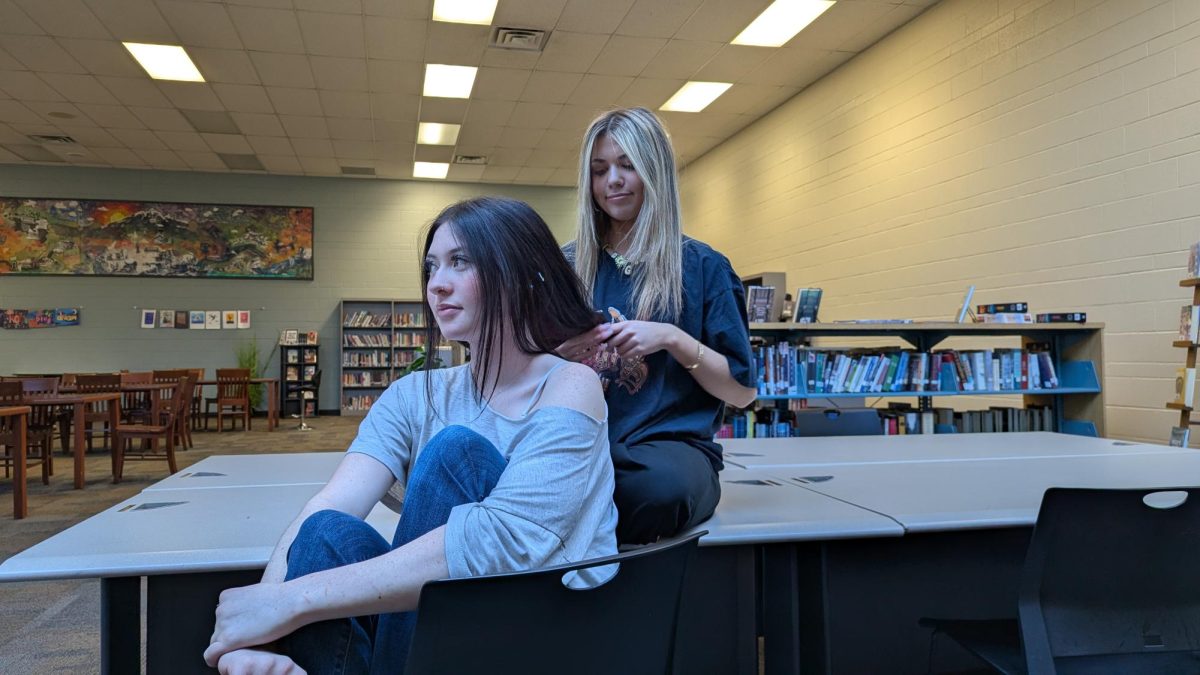 Gracie Esterline (12) practices braiding hair on Kelsi VerVaecke (12) in the MSHS Media Center on March 17.